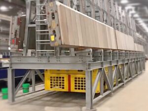 Mule meccanico giallo e nero per il trasporto di lastre di cemento prefabbricate, supportato da una struttura metallica grigia, in un impianto industriale
